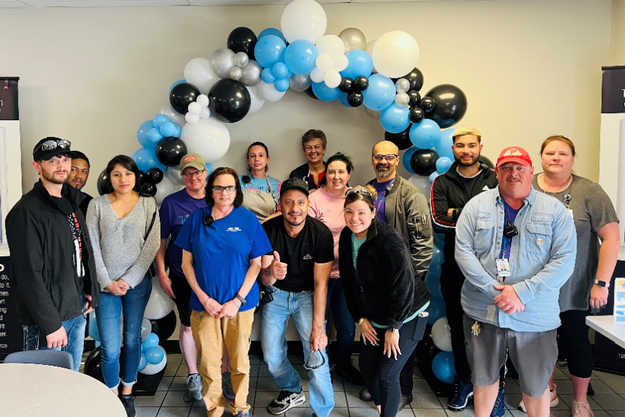 Comfort Bilt and Larson Manufaturing employees stand in front of a blue , black and white balloon arch at the Comfort Bilt Building. 